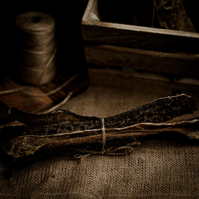  A bundle of Manx tripe sticks tied with string, presented on a fabric surface with a spool of string and a wooden box in the background.