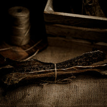  A bundle of Manx tripe sticks tied with string, presented on a fabric surface with a spool of string and a wooden box in the background.